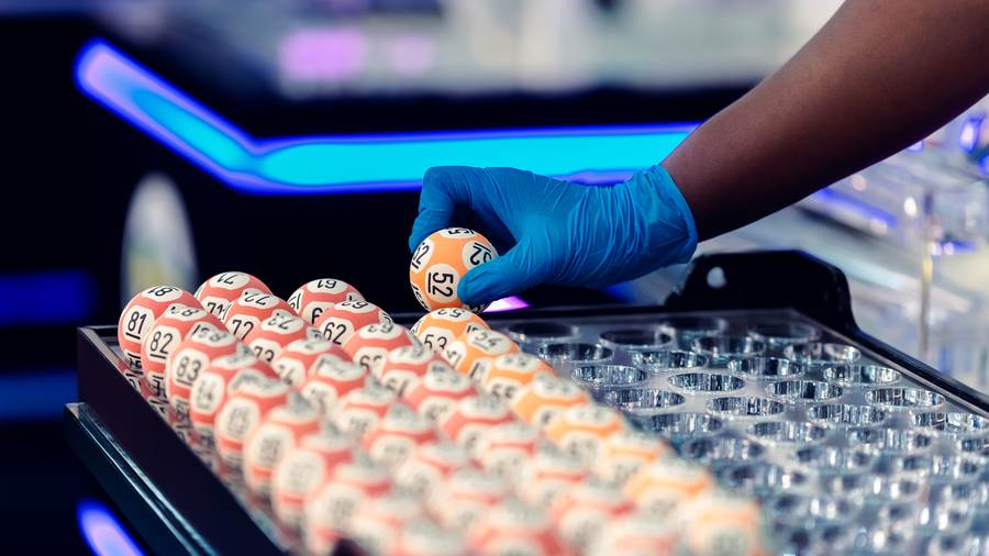 A gloved hand placing numbered balls into the tray before a draw