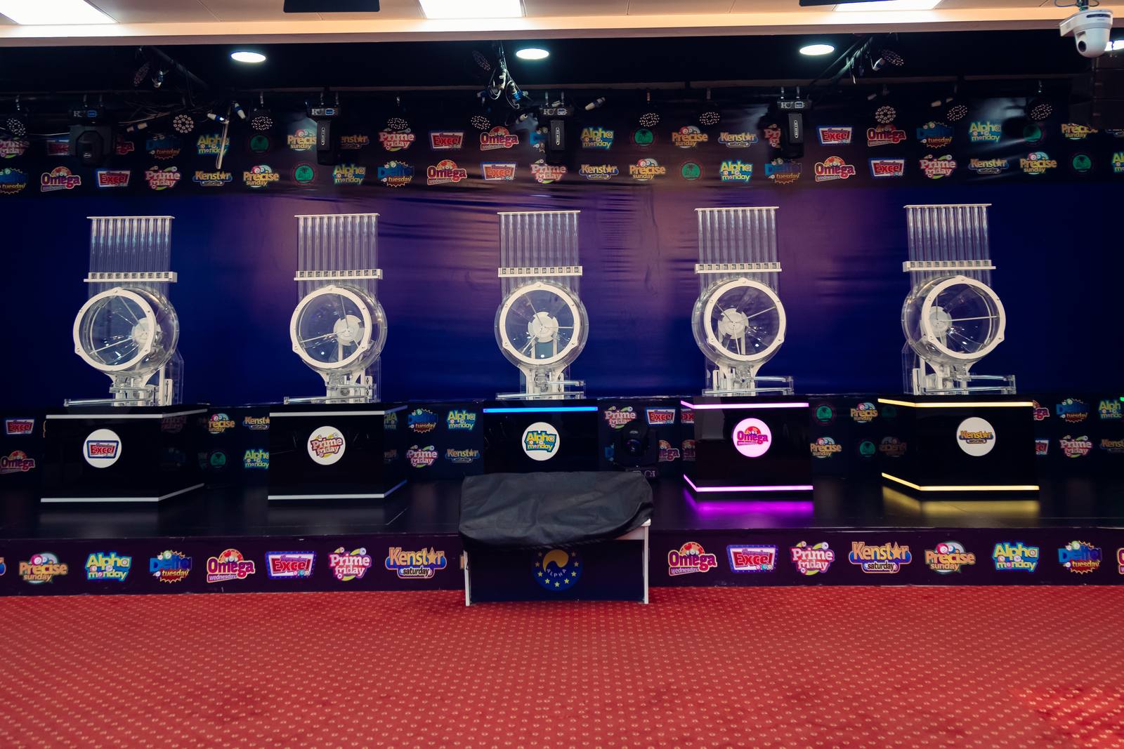 Draw machines lined up on the Alpha Lotto studio stage, each lit in its game's colour